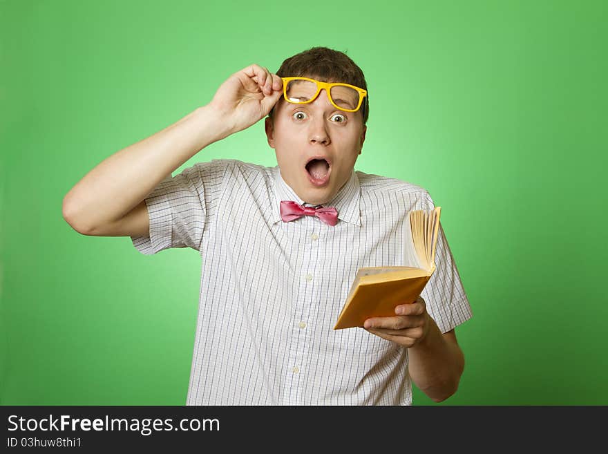 Young attractive man in a shirt and yellow glasses, bow tie on a green background reads the yellow book. Bookworm. Young attractive man in a shirt and yellow glasses, bow tie on a green background reads the yellow book. Bookworm