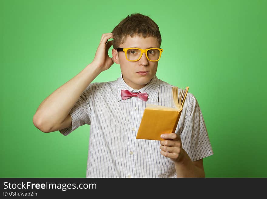 Young attractive man in a shirt and yellow glasses, bow tie on a green background reads the yellow book. Bookworm. Young attractive man in a shirt and yellow glasses, bow tie on a green background reads the yellow book. Bookworm