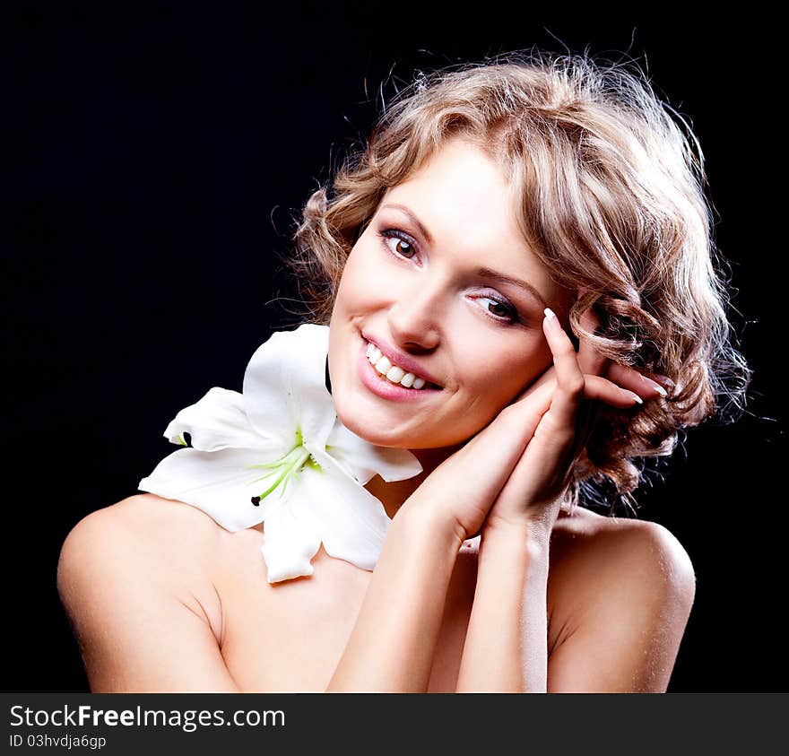 Beautiful young blond woman  with a lily in her hair, against black background