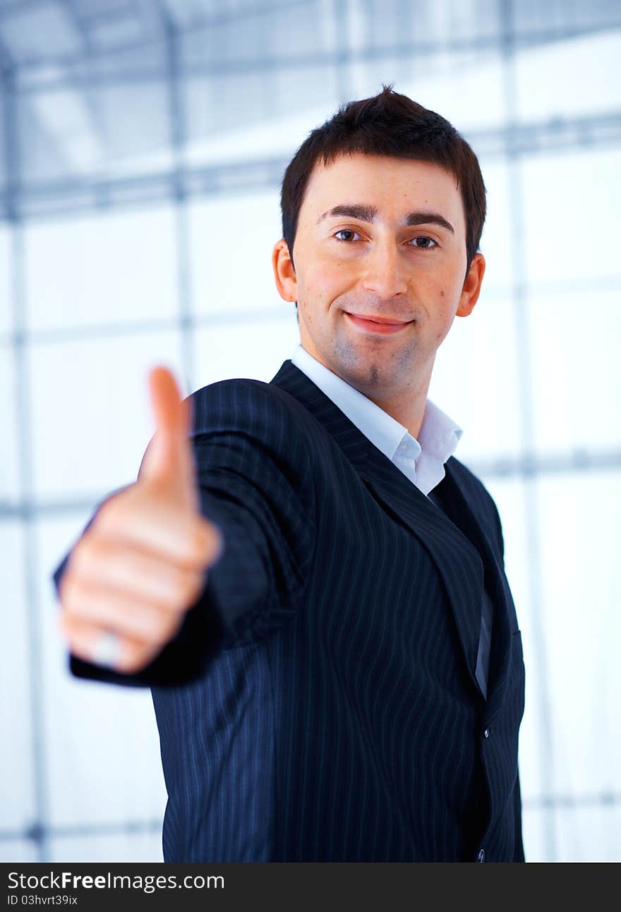 Happy handsome business man giving you a thumbs up sign against windows. Happy handsome business man giving you a thumbs up sign against windows.