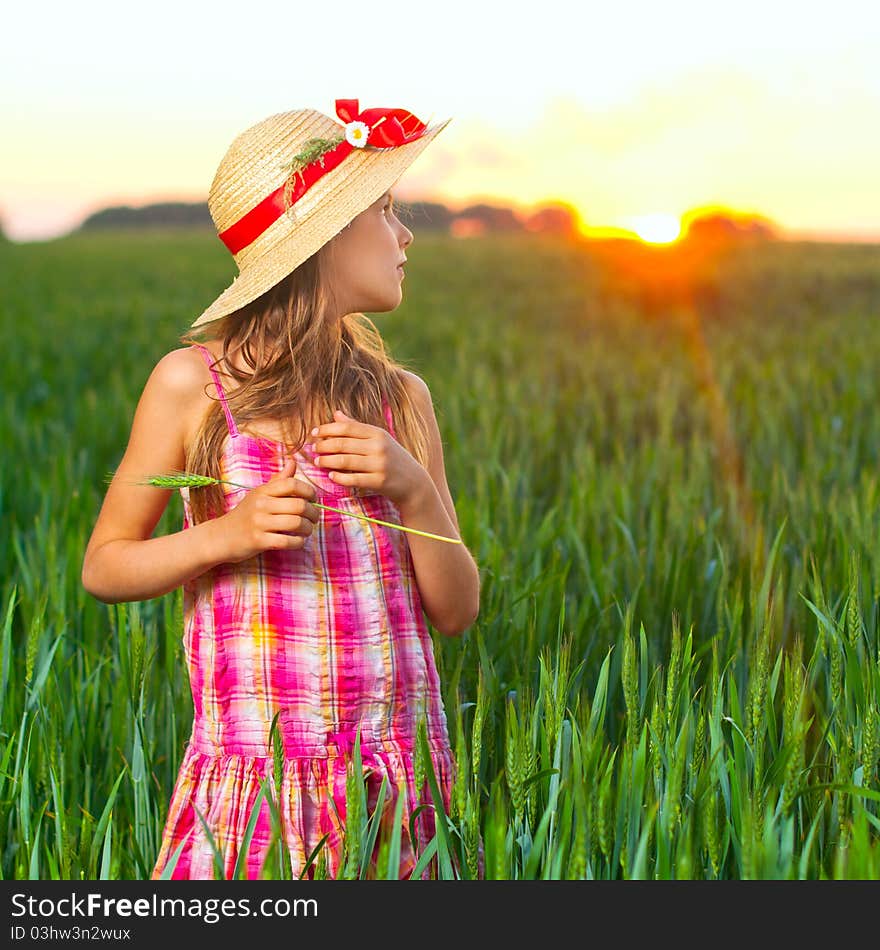 Cute girl in the straw hat with red ribbon on green wheat. Cute girl in the straw hat with red ribbon on green wheat.