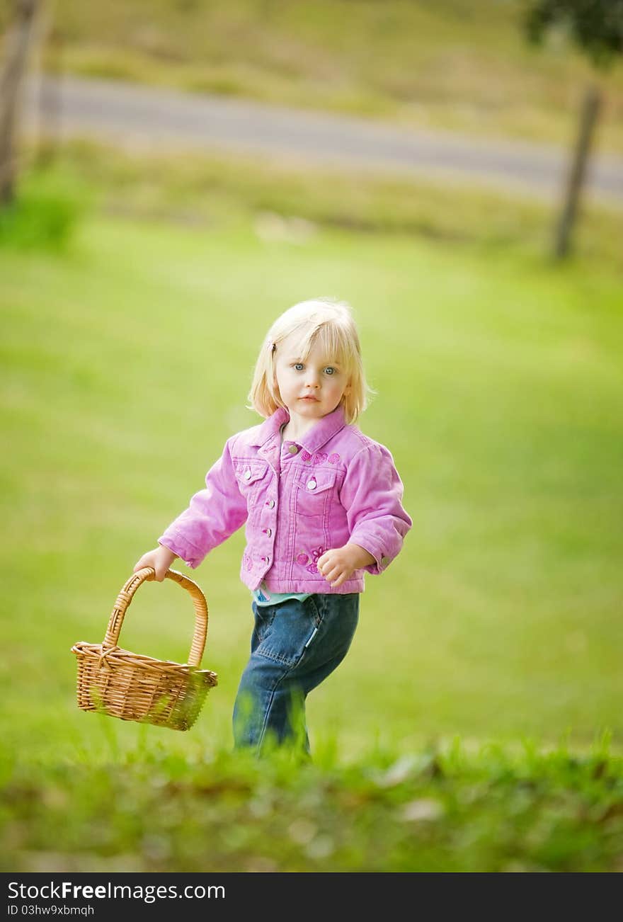 A cute little girl is holding a basket at the top of a hill. Selective focus has been used. The little girl looks relaxed and is looking at the camera. A cute little girl is holding a basket at the top of a hill. Selective focus has been used. The little girl looks relaxed and is looking at the camera.