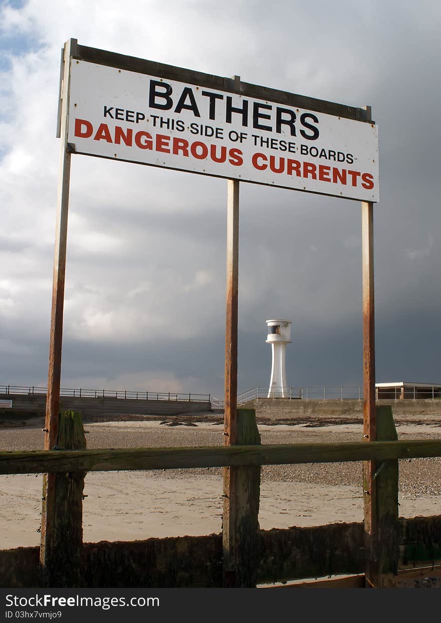 A warning sign to bathers on a beach out of season, against a stormy sky with a lighthouse in the background. A warning sign to bathers on a beach out of season, against a stormy sky with a lighthouse in the background.