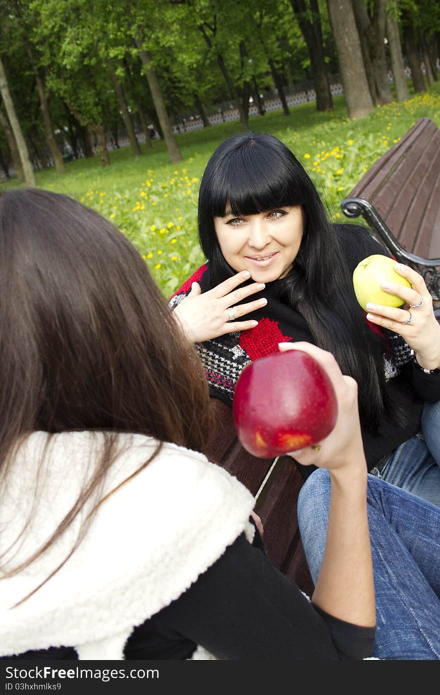 Mother and daughter in a park sitting on a wooden bench eating apples