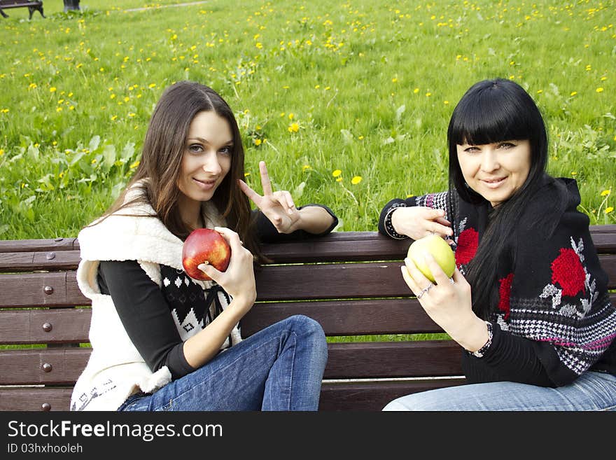 Mother and daughter in a park sitting on a wooden bench eating apples