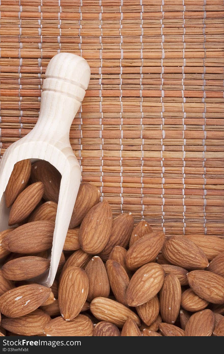 Nuts Almond are scattered as a background on a wooden mat.