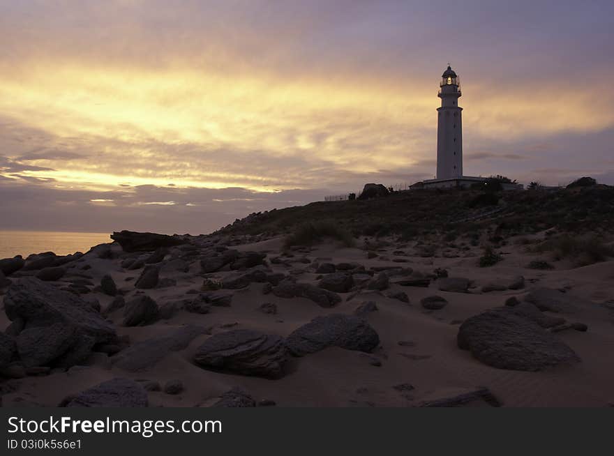 A photo of a lighthouse taken whilst the sun was setting from the beach making everything look like a silhouette. A photo of a lighthouse taken whilst the sun was setting from the beach making everything look like a silhouette