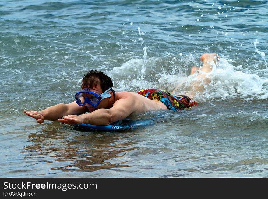 A man wears a diving mask while body boarding at the beach.