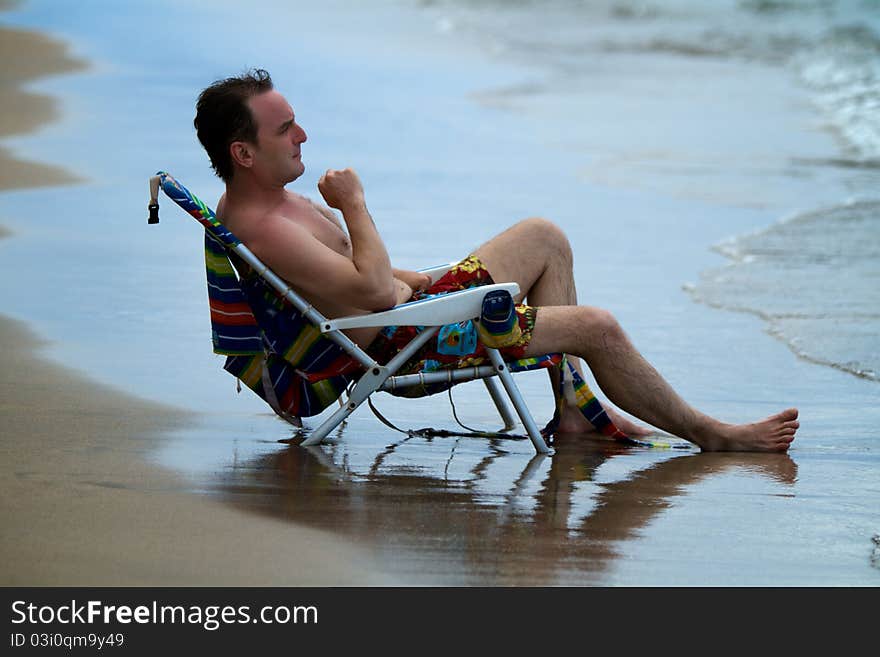 A man is deep in thought while sitting in a lawn chair at the edge of the shore at a Maul beach.