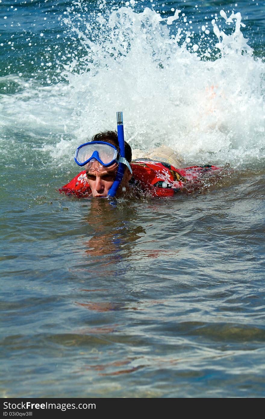 A man snorkels in his Hawaiian print shirt and creates a large splash as he swims in the ocean. A man snorkels in his Hawaiian print shirt and creates a large splash as he swims in the ocean.