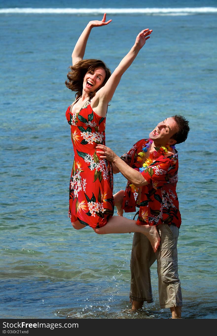 An excited couple on vacation frolic in the waves on a beach in Maui, Hawaii.