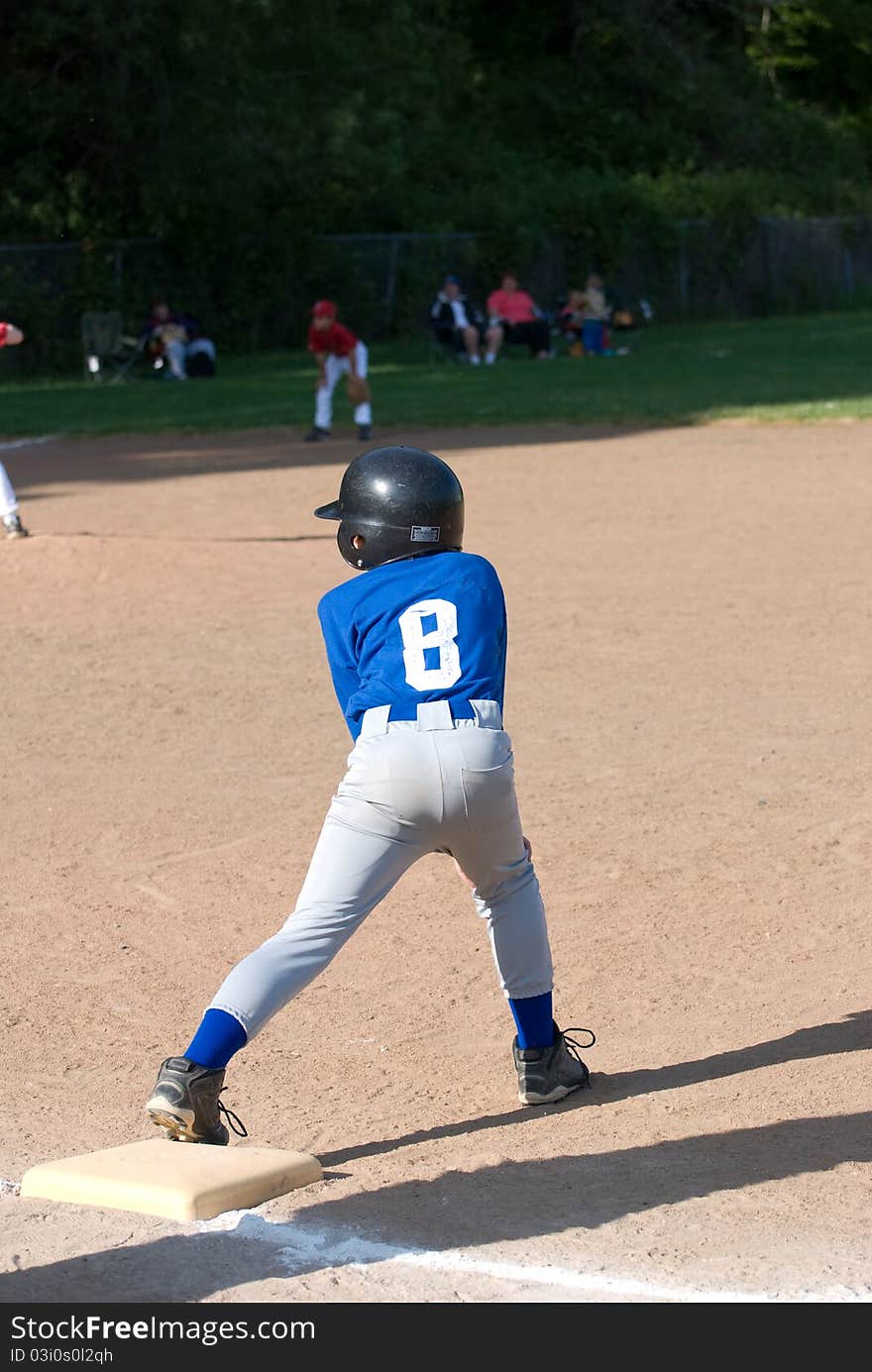 A Little League player wearing a blue and gray uniform with a black helmet stretches off the base getting ready to run in a game in Salem, Oregon in 2010. A Little League player wearing a blue and gray uniform with a black helmet stretches off the base getting ready to run in a game in Salem, Oregon in 2010