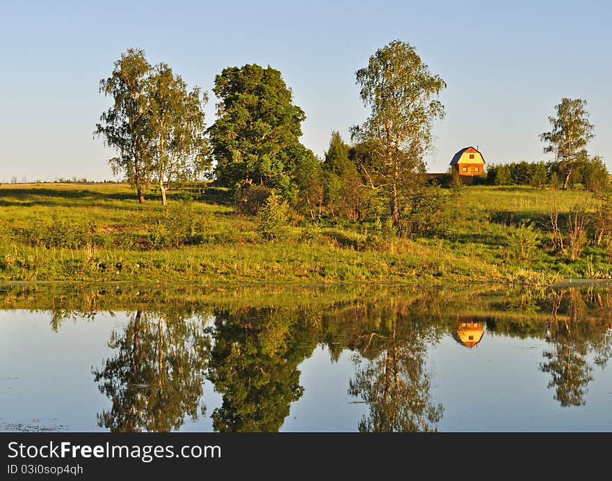 Country summer landscape with small house on lake bank and trees reflections, evening. Country summer landscape with small house on lake bank and trees reflections, evening