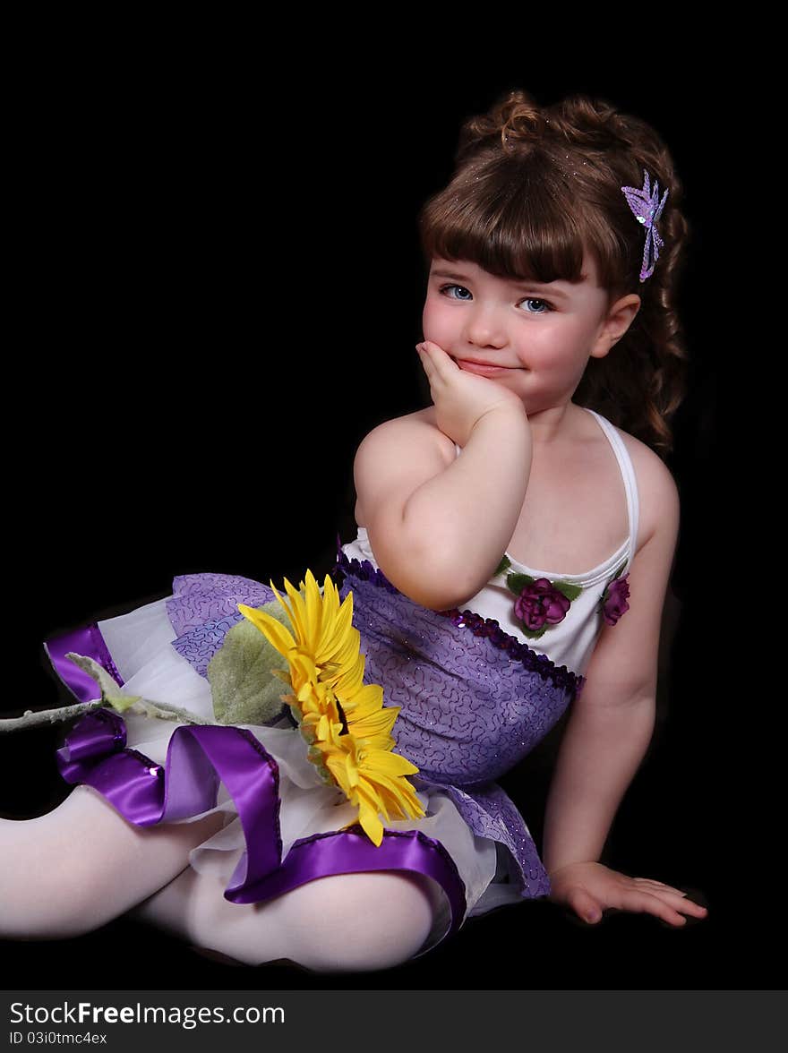 Smiling sweet little girl in purple and white ballet outfit sitting with sunflower. isolated on black. Smiling sweet little girl in purple and white ballet outfit sitting with sunflower. isolated on black