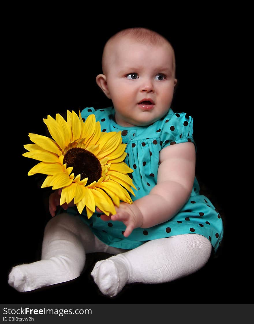 Beautiful infant girl in polka dot dress sitting with large golden sunflower. isolated on black. Beautiful infant girl in polka dot dress sitting with large golden sunflower. isolated on black