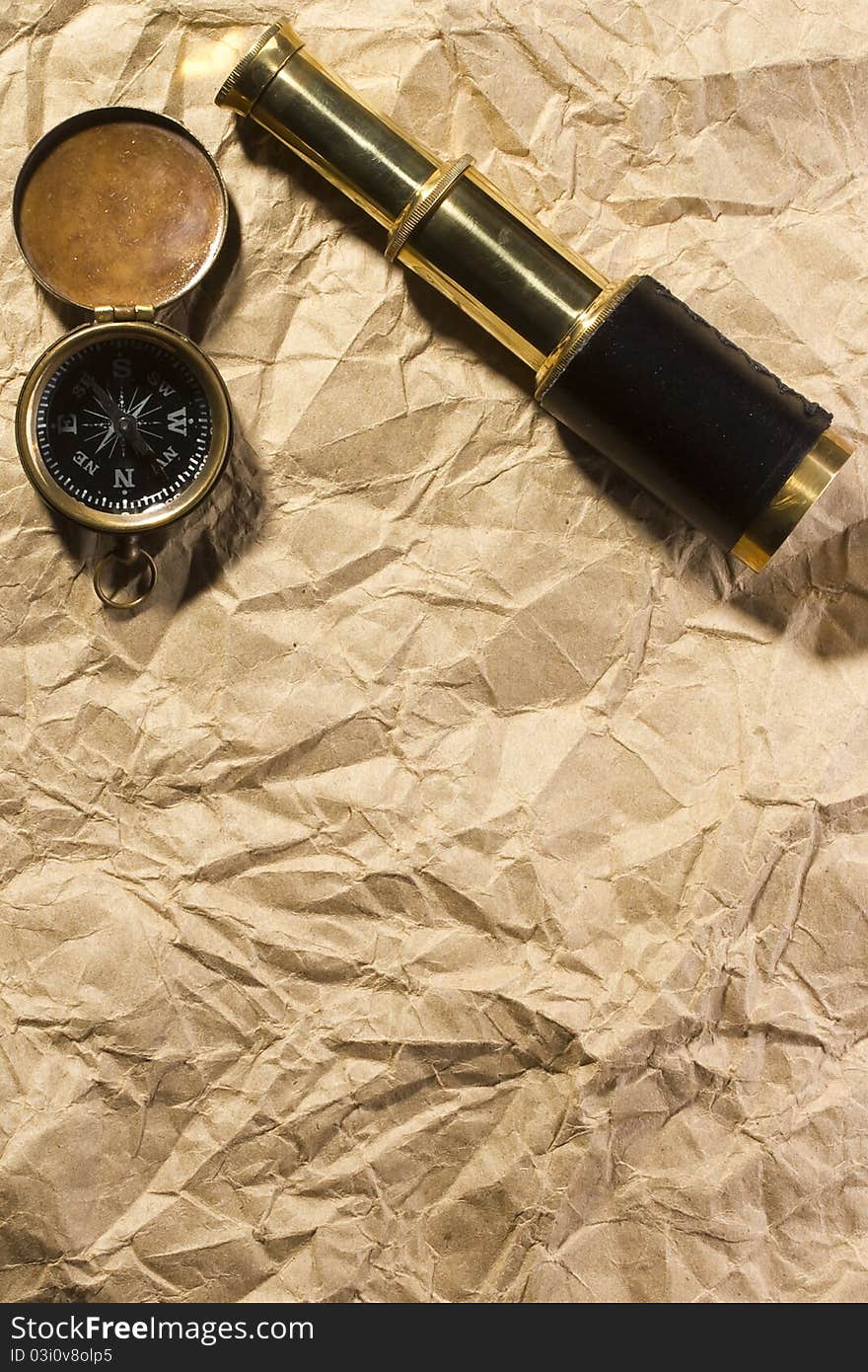 A golden compass and a spyglass laying on an old wrinkled brown paper that can serve as a background for a message or a drawing of a map. A golden compass and a spyglass laying on an old wrinkled brown paper that can serve as a background for a message or a drawing of a map.