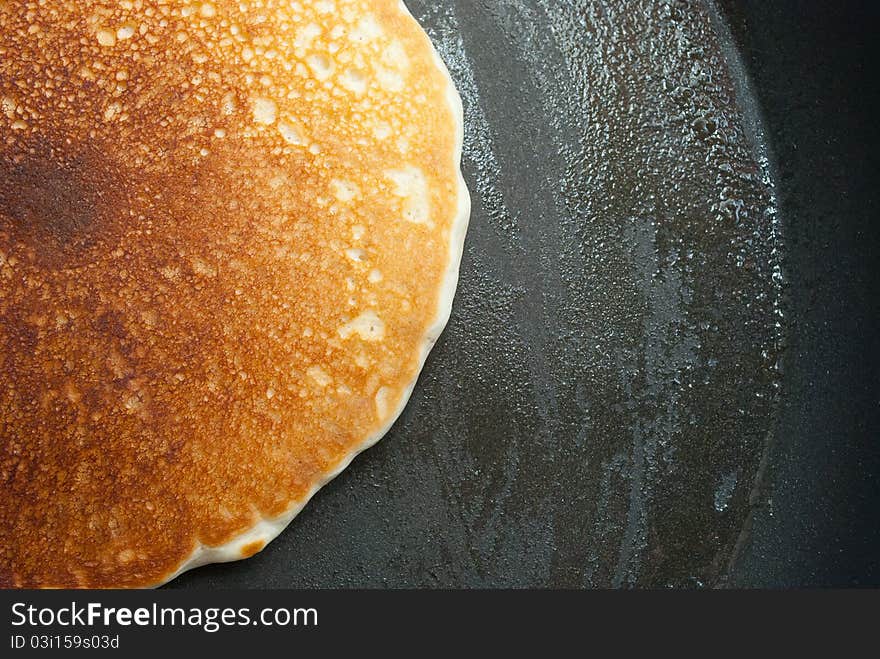 A pancake in a buttered frying pan. A pancake in a buttered frying pan.