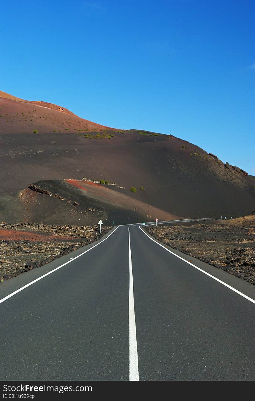 Quiet and empty road in the middle of the day at fool sun leading to Vulcan Timanfaya national park at Lanzarote Canary Islands. Quiet and empty road in the middle of the day at fool sun leading to Vulcan Timanfaya national park at Lanzarote Canary Islands