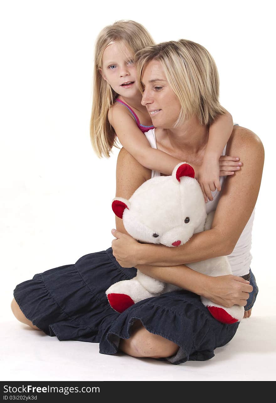 Attractive blonde mother and daughter, in a loving embrace, with a teddy bear. Attractive blonde mother and daughter, in a loving embrace, with a teddy bear.