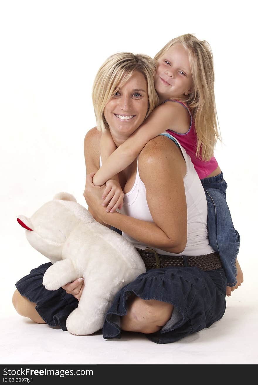 Attractive blonde mother and daughter, in a loving embrace, with a teddy bear. Attractive blonde mother and daughter, in a loving embrace, with a teddy bear.