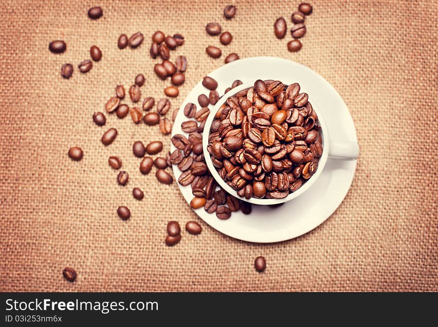 Cup with coffee beans on fabric texture background