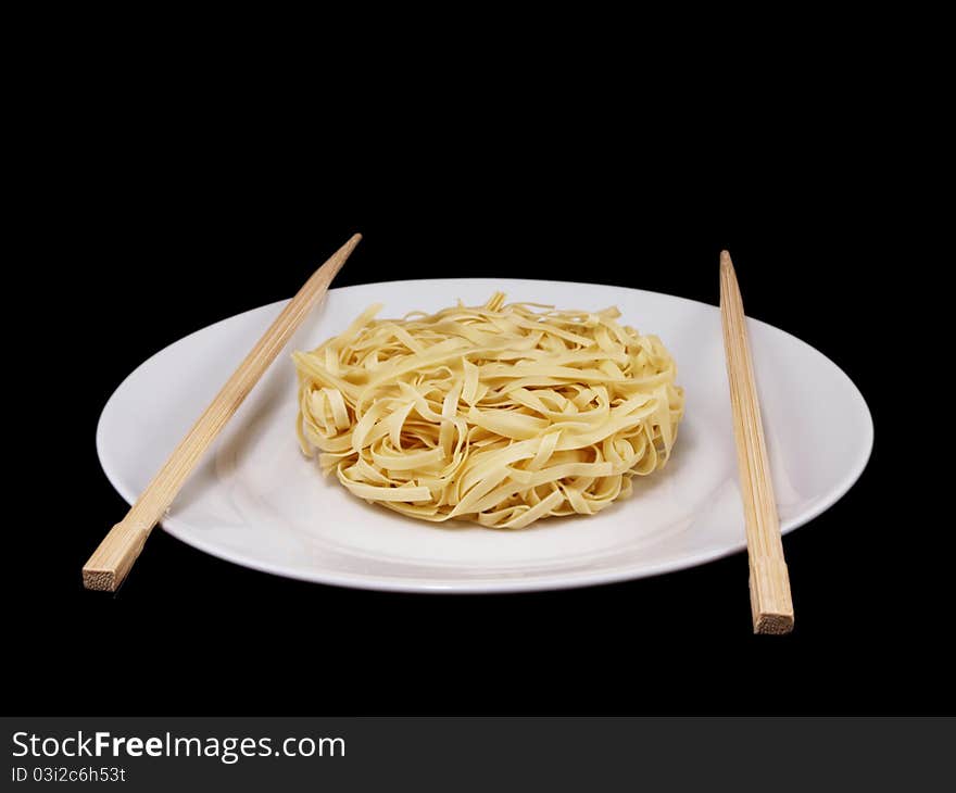 Uncooked noodles, on white plate, with chopsticks, isolated towards black background