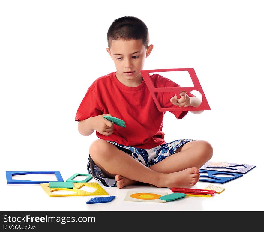 A kindergarten boy attempting to match colorful shapes with puzzel frames. Isolated on white. A kindergarten boy attempting to match colorful shapes with puzzel frames. Isolated on white.