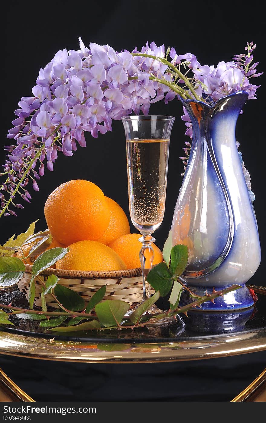 On a round little table a basket with oranges, white wine and a flower Wisteria. On a round little table a basket with oranges, white wine and a flower Wisteria.