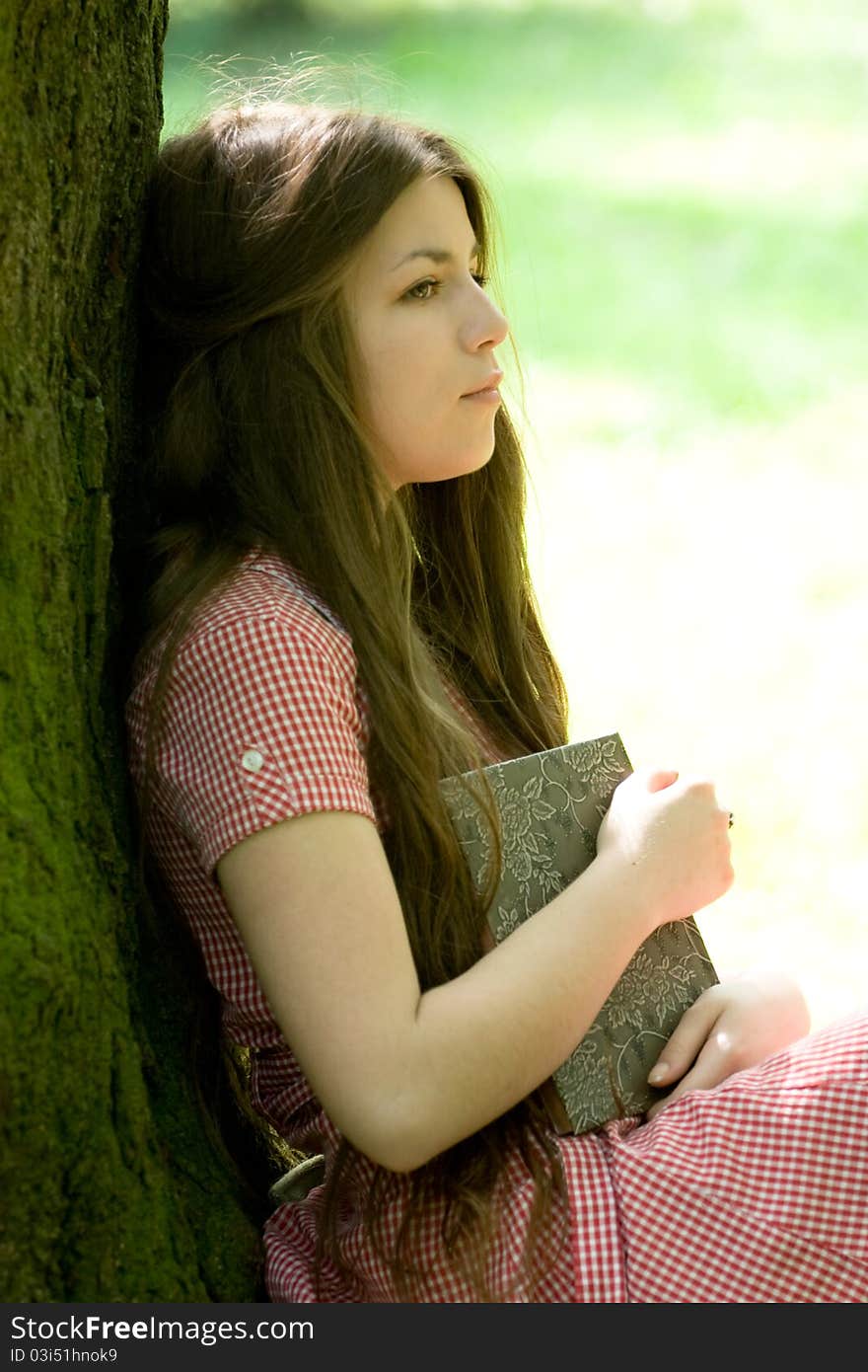 Attractive girl is sitting with book in the park and thinking or dreaming. Attractive girl is sitting with book in the park and thinking or dreaming