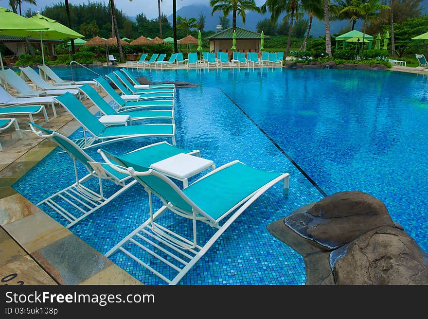 Turquoise chairs sitting in a deep blue swimming pool surrounded by green umbrellas at an upscale resort in Kauai, Hawaii. Turquoise chairs sitting in a deep blue swimming pool surrounded by green umbrellas at an upscale resort in Kauai, Hawaii