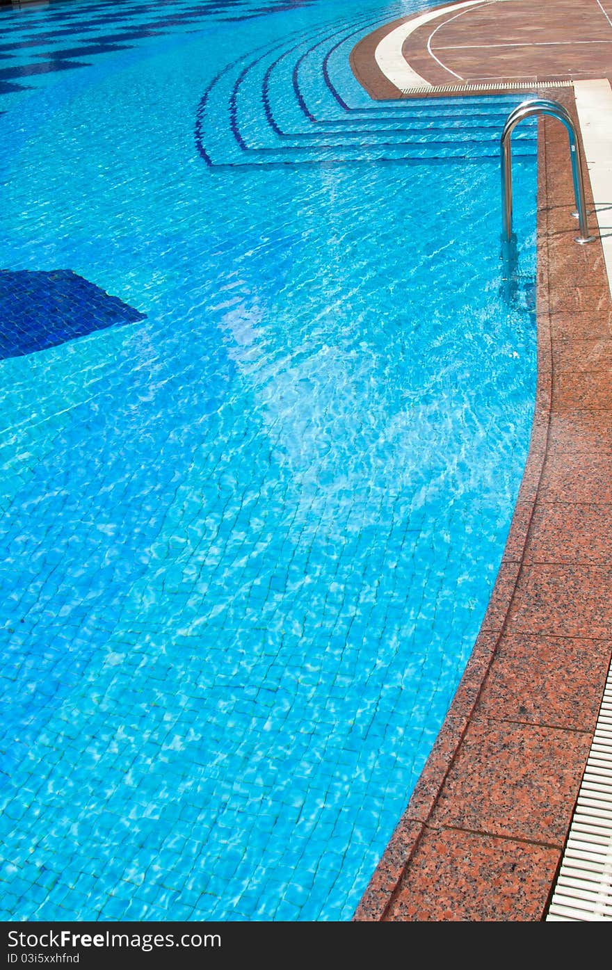 A portrait of blue tile swimming pool with steps and staircase entrance with marble edging. A portrait of blue tile swimming pool with steps and staircase entrance with marble edging