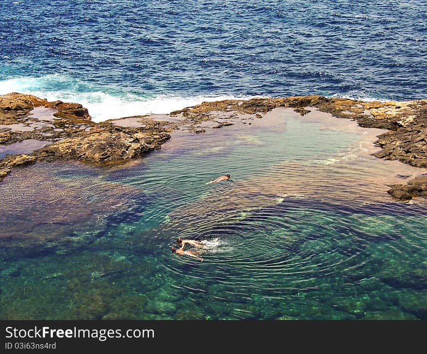 People diving in a natural basin in the rocks coastline of Lanzarote