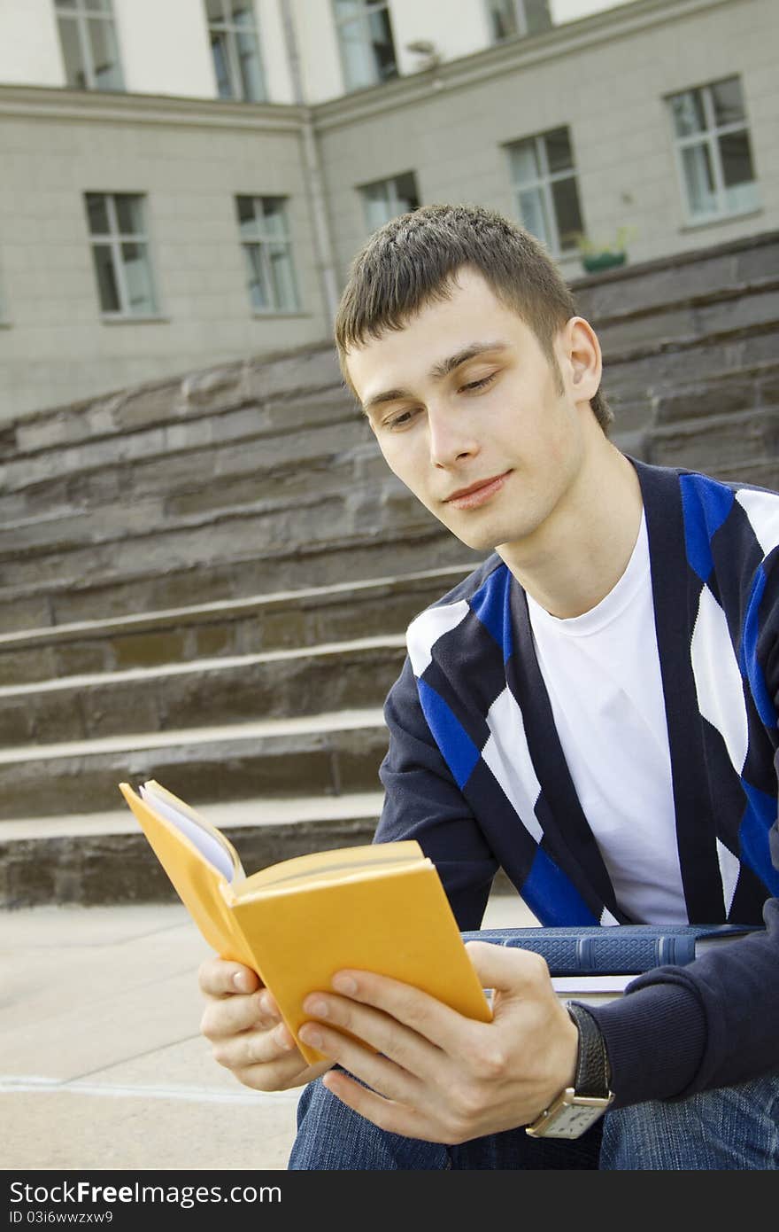 Closeup of an attractive male student on campus sits on the stairs with books. Closeup of an attractive male student on campus sits on the stairs with books