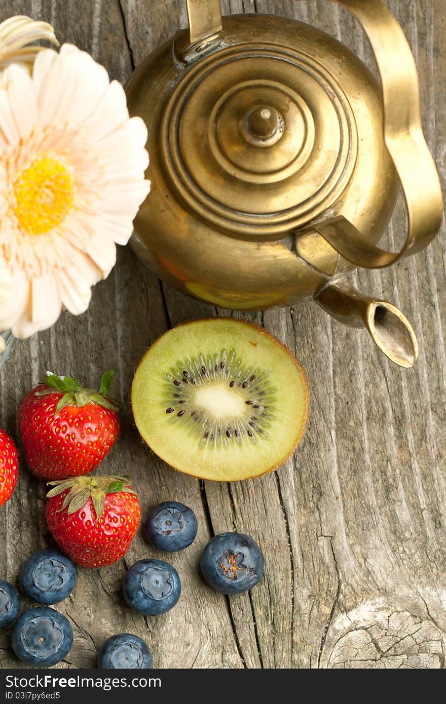 Top view on fresh strawberries, blueberries and kiwi with old vintage teapot on old wooden table. Top view on fresh strawberries, blueberries and kiwi with old vintage teapot on old wooden table