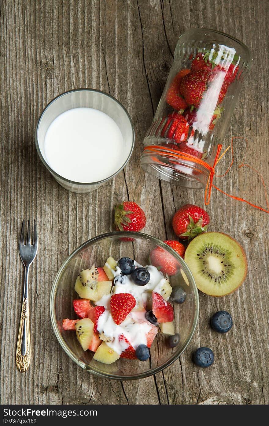 Top view on bowl of fruit salad with fresh strawberries, blueberries and kiwi with glass of milk on old wooden table table. Top view on bowl of fruit salad with fresh strawberries, blueberries and kiwi with glass of milk on old wooden table table