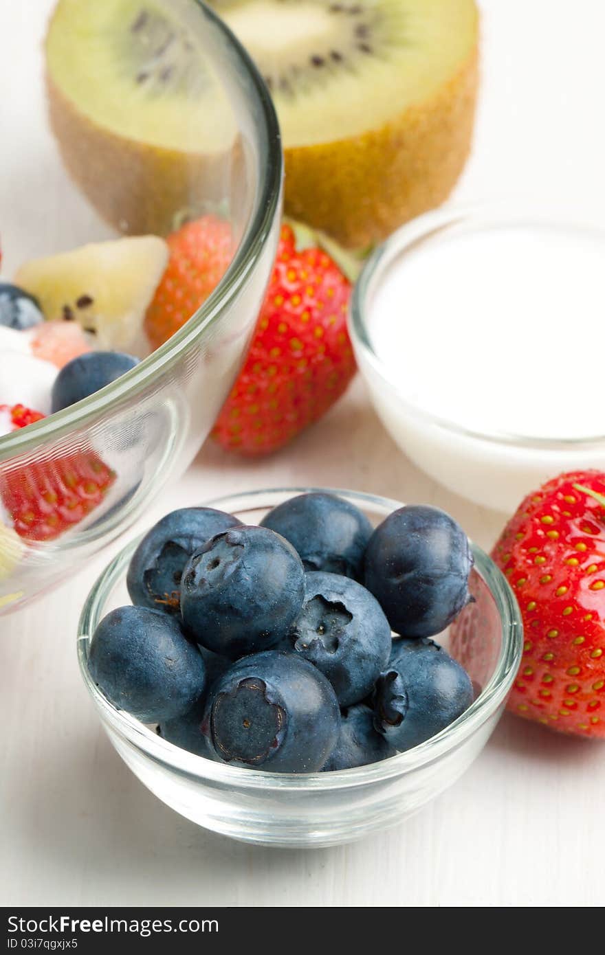 Glass bowl of fresh strawberries, blueberries and kiwi with whipped cream on white table. Glass bowl of fresh strawberries, blueberries and kiwi with whipped cream on white table