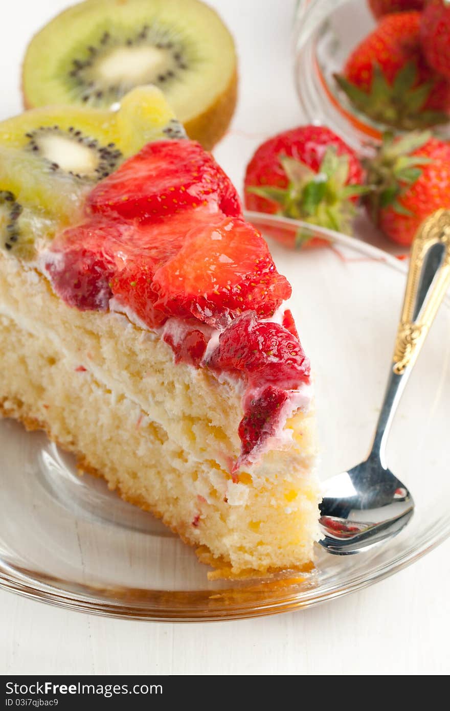 Piece of homemade fruit cake with strawberries and kiwi on white wooden table