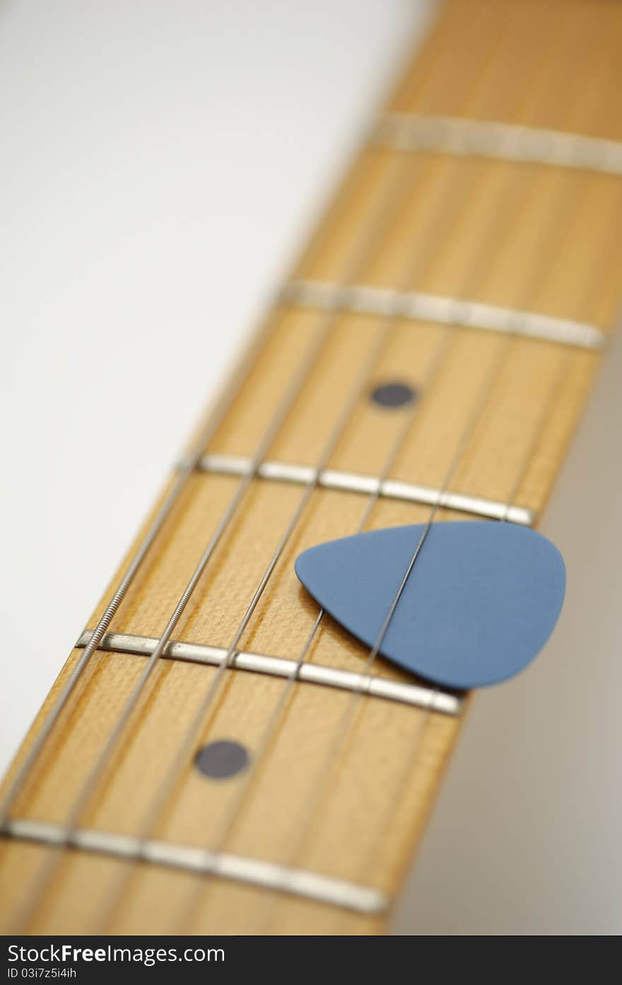 Blue guitar pick held between three strings on the neck of an electric guitar with maple fretboard.