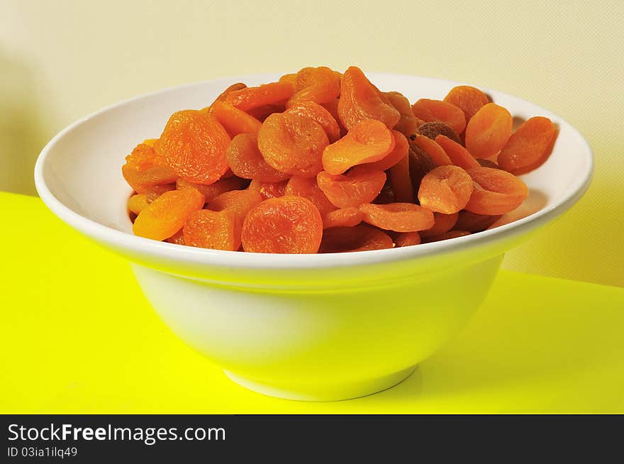 Dried apricots are in a deep white plate against a yellow background