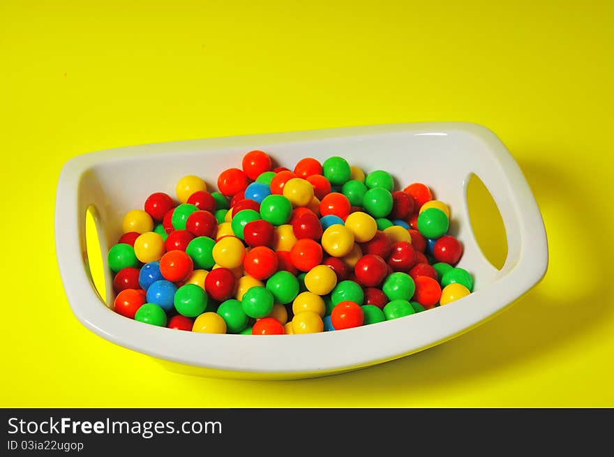 Children's chewing gum in the form of colored balls lie in a deep white plate. Children's chewing gum in the form of colored balls lie in a deep white plate