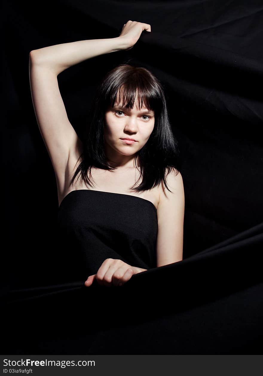 The woman in a dark dress against a dark background. The woman in a dark dress against a dark background