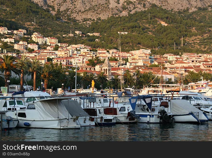 Yaht port is placing near the old town of Makarska, Croatia. Beautiful colors of the sunset and old ancient roofs on it. Panoramic view. Yaht port is placing near the old town of Makarska, Croatia. Beautiful colors of the sunset and old ancient roofs on it. Panoramic view.