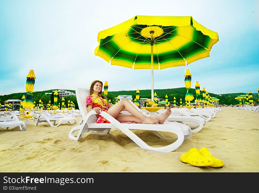 Beautiful happy woman in colourful clothes is laying on the sunbed on the beach under umbrella. Wide angle shot. Beautiful happy woman in colourful clothes is laying on the sunbed on the beach under umbrella. Wide angle shot.