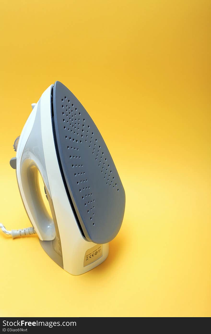 Closeup of gray modern electric iron on yellow background