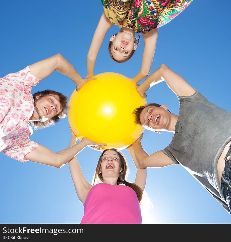 Group of young people hold big yellow ball across blue sky. Group of young people hold big yellow ball across blue sky