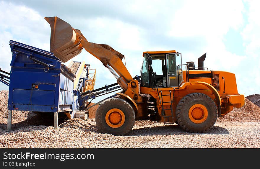 A yellow excavator load a conveyors for making and moving industrial gravel. A yellow excavator load a conveyors for making and moving industrial gravel