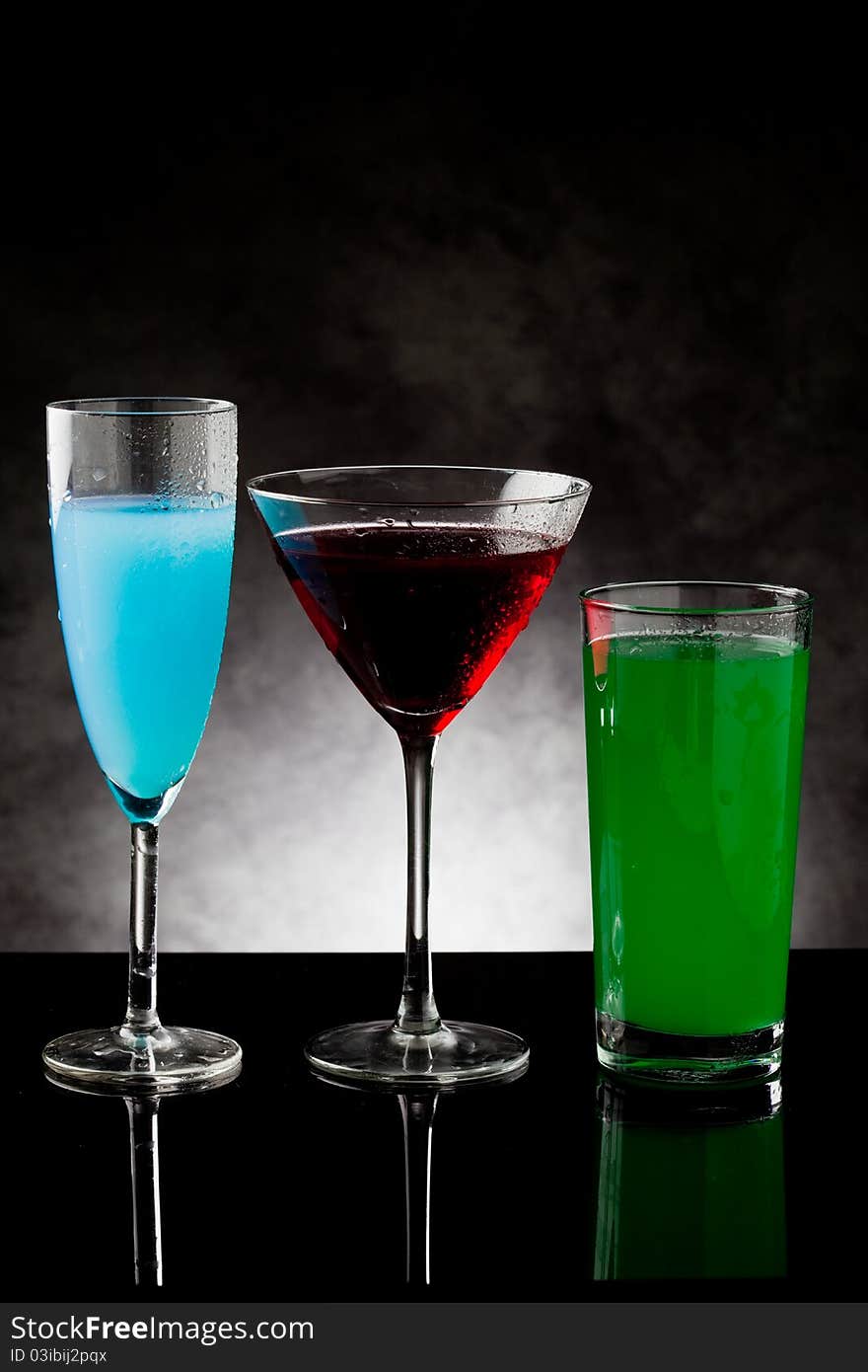 Photo of three cocktails on black glass counter with grey lighted background