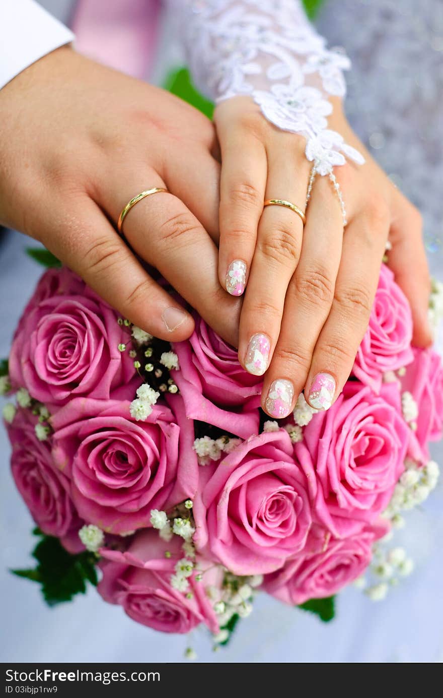 Hands of bride and groom with wedding rings over the bridal bouquet. Hands of bride and groom with wedding rings over the bridal bouquet