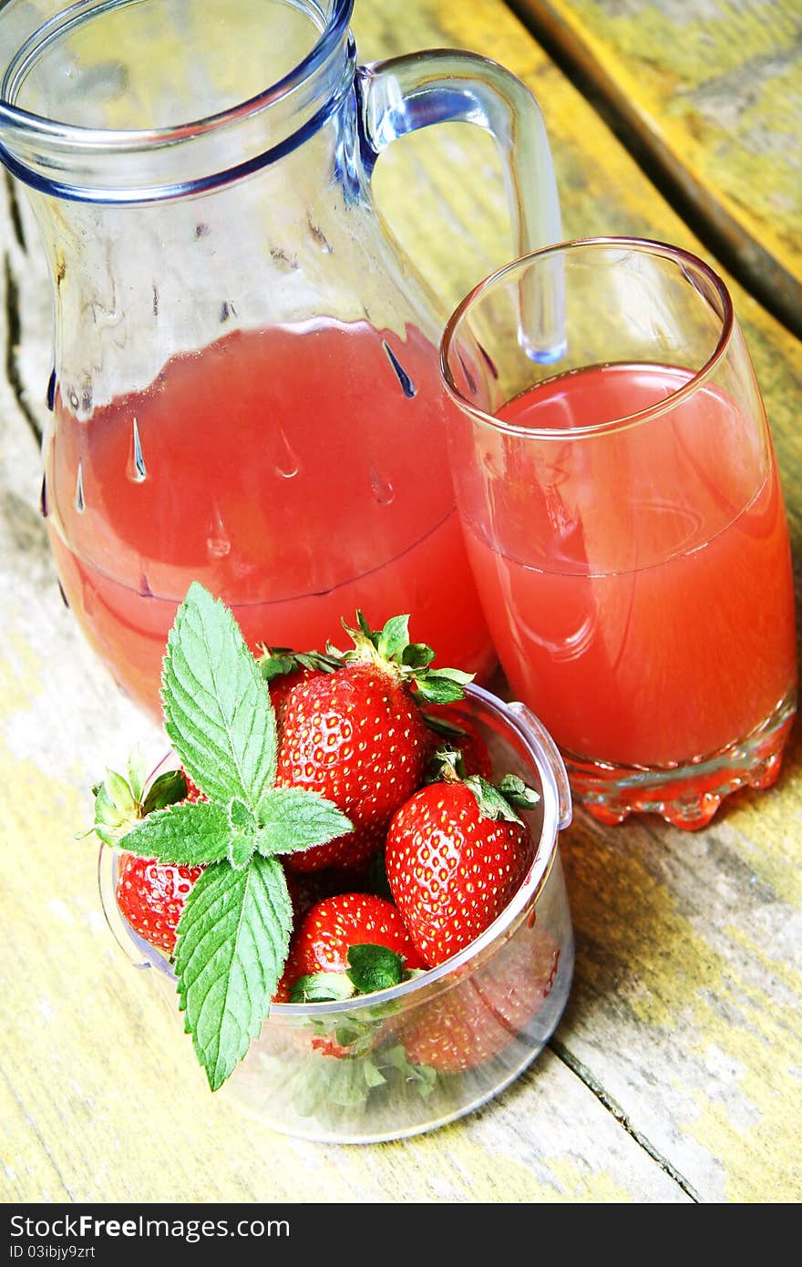 Strawberry juice in a glass pitcher and glass, next to a bowl of strawberries on a wooden table.Top view. Strawberry juice in a glass pitcher and glass, next to a bowl of strawberries on a wooden table.Top view