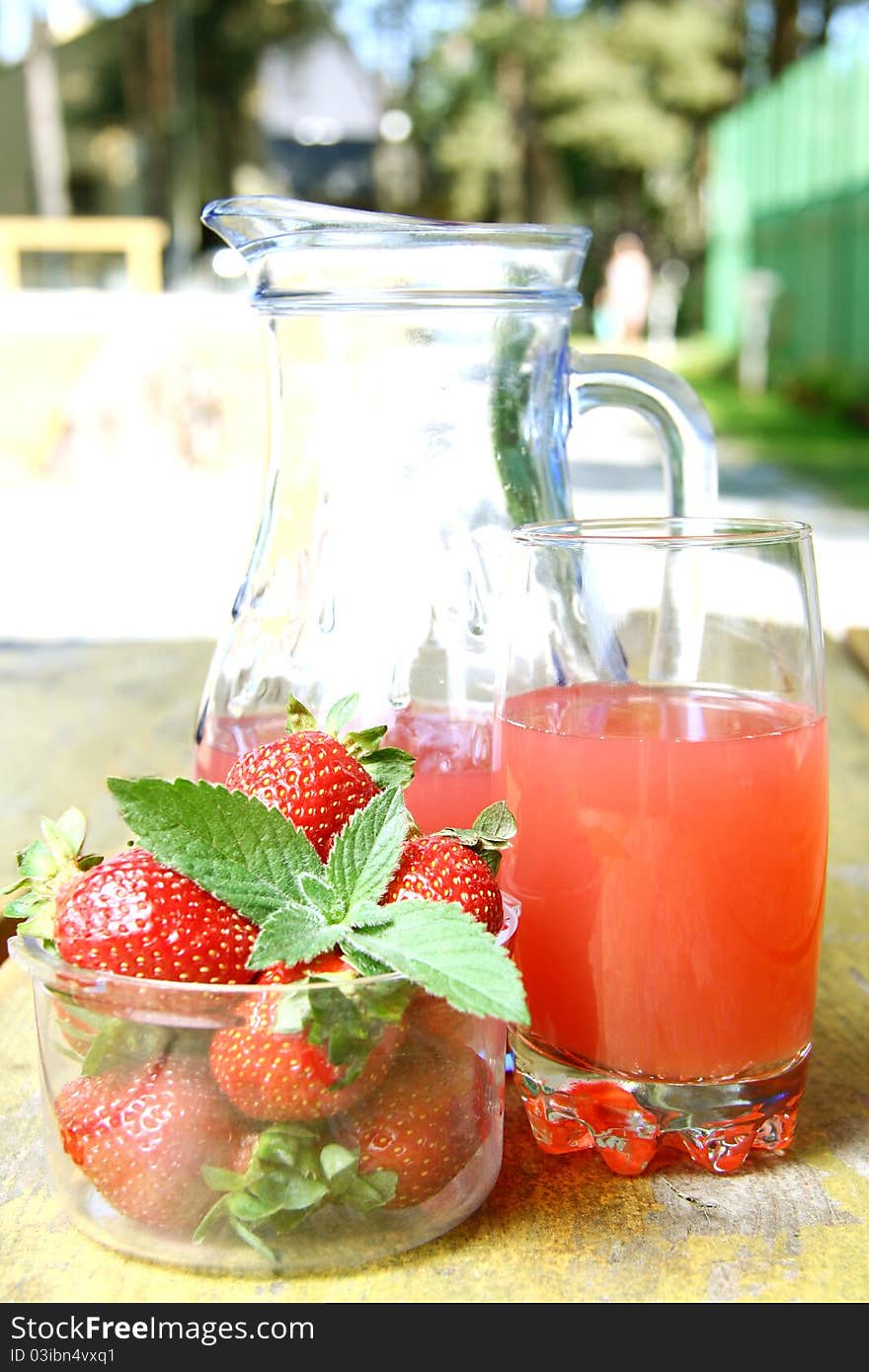 Strawberry juice in a glass pitcher and glass, next to a bowl of strawberries on a wooden table. Strawberry juice in a glass pitcher and glass, next to a bowl of strawberries on a wooden table